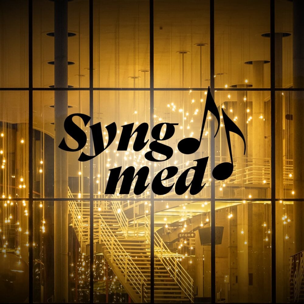 Glassfasade med refleksjon av hengende lys, trapp på innsiden og ordene "Syng med" overlagt, med musikalske toner integrert i teksten.