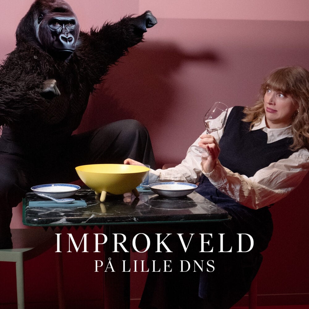 En person i gorillakostyme poserer med armene hevet ved siden av en forskrekket kvinne som holder et vinglass ved et bord dekket med skåler. Teksten lyder "IMPROKVELD PÅ LILLE DNS".