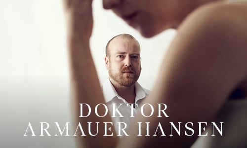 En mann med alvorlig ansiktsuttrykk står i bakgrunnen, mens en uskarp person står i forgrunnen. Teksten lyder "Doktor Armauer Hansen.