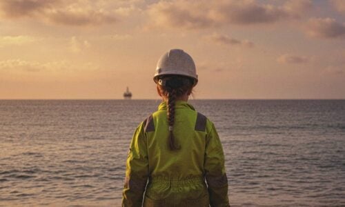 Et barn i gul beskyttelsesdrakt og hjelm står på en klippekant vendt mot havet, med en offshoreplattform synlig i det fjerne. Teksten lyder "Ildens Historie Demian Vitanza.