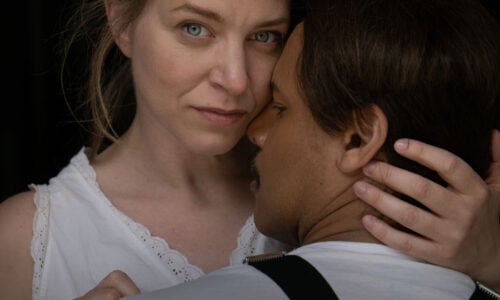 Forestillingsplakat, Frøken Julie. En kvinne i en hvit topp ser inn i kameraet, mens en mann med bukseseler står med ryggen til og holder rundt henne. Teksten lyder: «Frøken Julie, August Strindberg.».