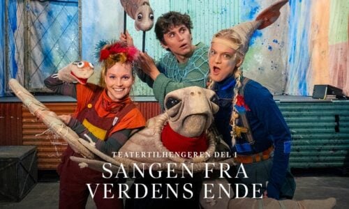 Tre utøvere i fargerike kostymer poserer med store dyredukker på en scene med malt bakteppe. Den norske teksten lyder "Teatertilhengeren del 1 Sangen fra Verdens Ende".