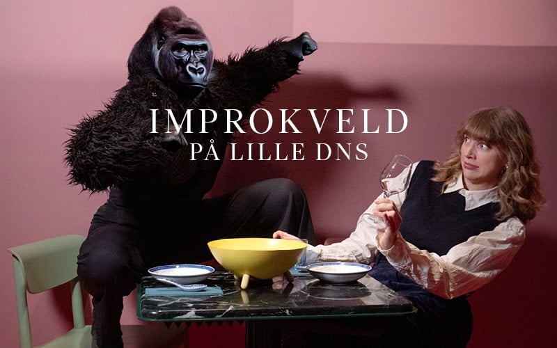 En person i gorillakostyme poserer med hevet arm ved siden av en kvinne som holder et vinglass ved et bord dekket med skåler, mot en rosa bakgrunn. Teksten lyder "IMPROKVELD PÅ LILLE DNS.