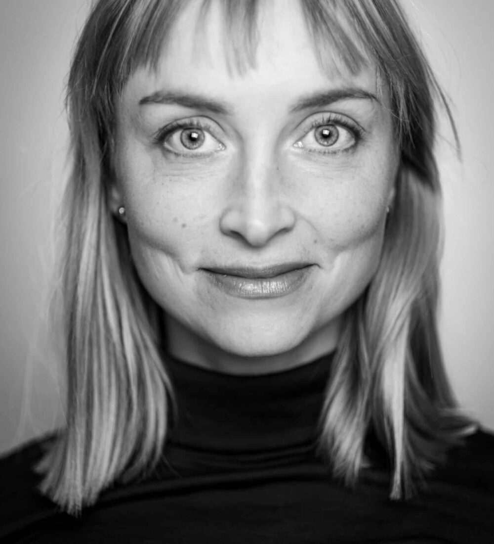 Svart-hvitt portrett av en kvinne med rett, skulderlangt hår, iført mørk rullekrage, som ser direkte inn i kameraet med et nøytralt uttrykk.