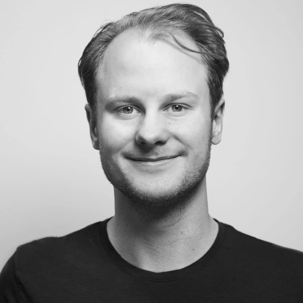 Smilende mann med kort hår mot en lys bakgrunn.