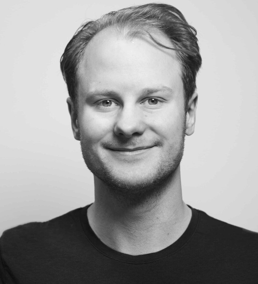 Smilende mann med kort hår mot en lys bakgrunn.