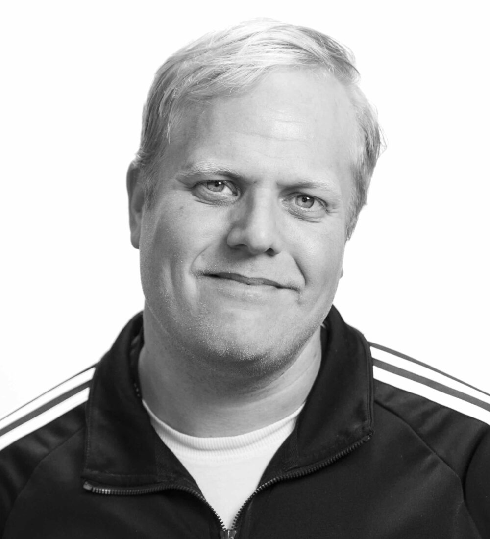 Harald Ottesen Nødtvedt En mann med kort, blondt hår, iført jakke med glidelås og hvite striper på skuldrene, ser inn i kameraet med et nøytralt uttrykk mot en hvit, ensfarget bakgrunn.