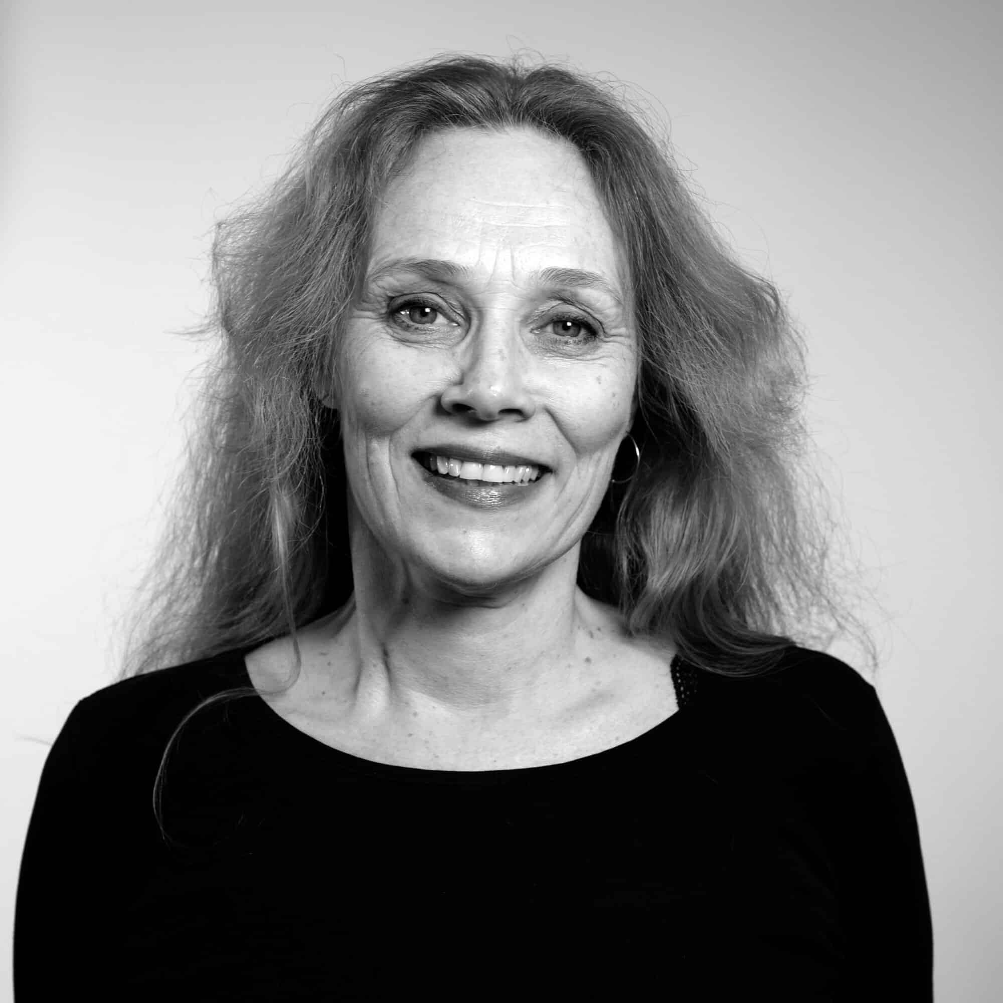 Et svart-hvitt portrett av en smilende middelaldrende kvinne med langt hår.