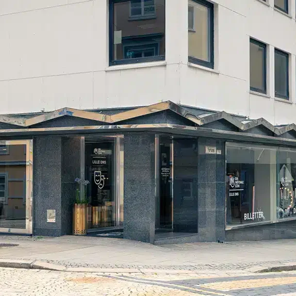 Utsikt fra gaten mot en hjørnebygning med store vinduer der det henger skilt for et ballett- og dansestudio; brosteinsbelagt fortau foran.
