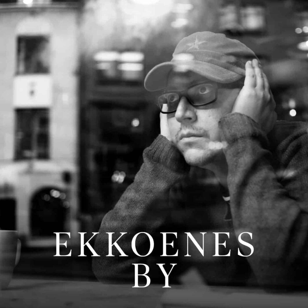 En person med briller og lue sitter med hendene på kinnene og ser ut av et vindu; teksten «EKKOENES BY» er lagt over bildet.