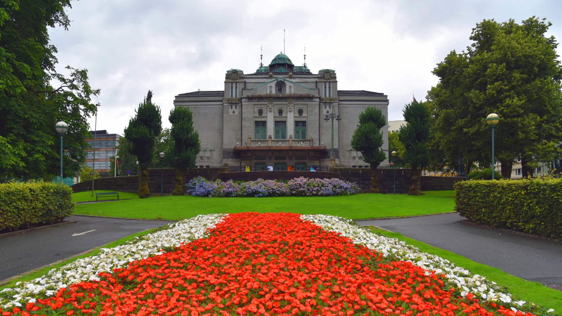 En symmetrisk utsikt over en storslått bygning med dekorative blomsterbed i forgrunnen.