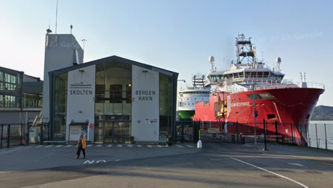 En person går utenfor inngangen til Skolten Internasjonale Terminal på Bergen Havn, med et stort rødt og hvitt skip ved kai like ved.