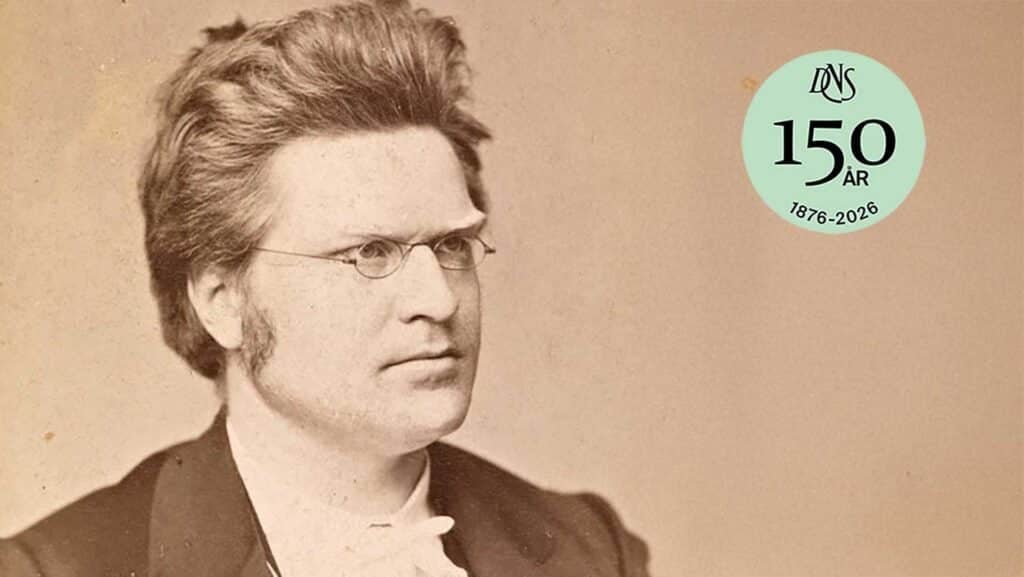 Sepiatonet portrett av en mann med briller og kinnskjegg, iført dress. I hjørnet står det