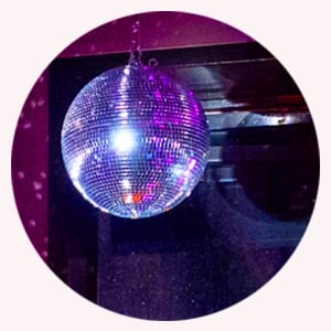 En sølvfarget discokule henger fra taket og reflekterer lilla og blått lys i det mørke rommet.