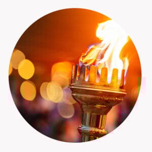 Nærbilde av en tent fakkel med metallholder som brenner med en lys oransje flamme mot en uskarp bakgrunn av varmt lys.