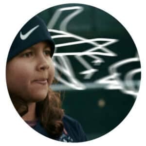 En ung person i blå Nike-lue står utendørs, med abstrakte hvite linjer og en uskarp bakgrunn bak seg.