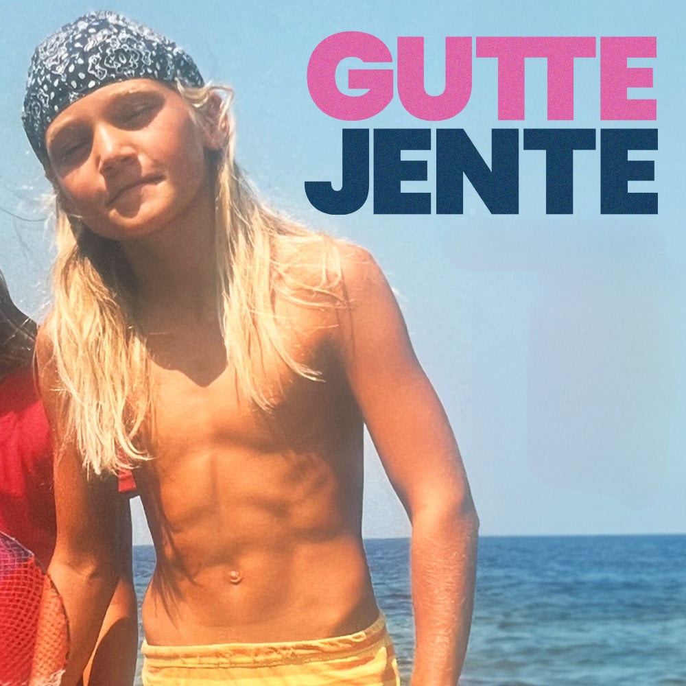 Et langhåret barn iført bandana og gule shorts står ved sjøen. Ordene «GUTTE JENTE» er skrevet med fet rosa og blå tekst øverst til høyre.