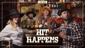 Fire personer med cowboyhatter og rutete skjorter står ved en bar med flere ølkraner, smiler og poserer. Teksten på bildet lyder: «HIT HAPPENS.».