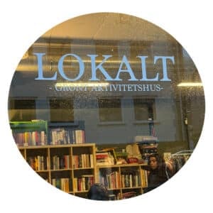 LOKALT GRØNT AKTIVITETSHUS" står det på et vindusskilt over bokhyller fylt med bøker og mennesker som sitter inne.