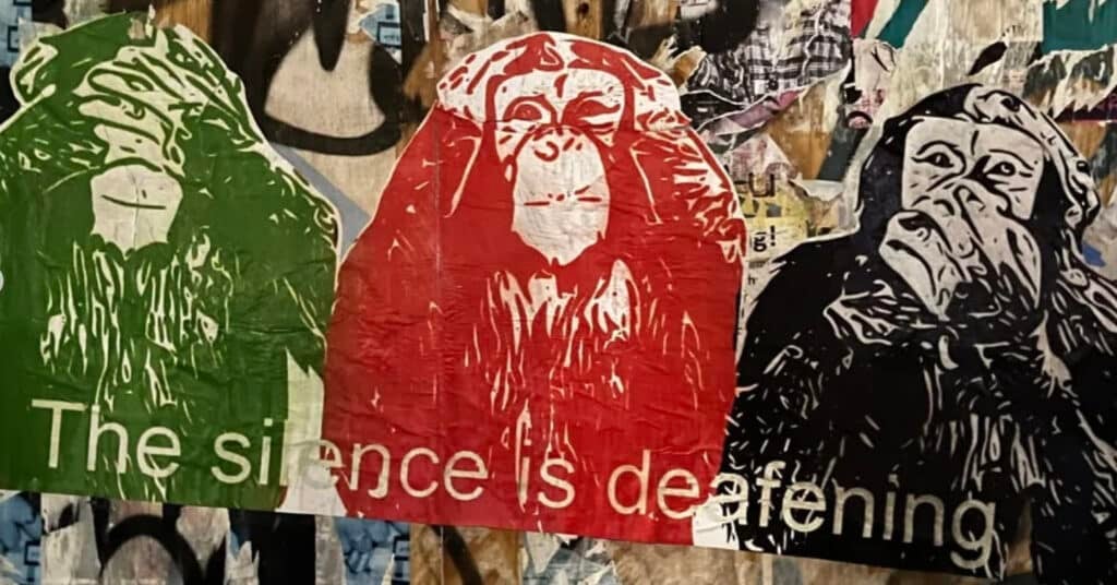 Tre stiliserte aper med hendene over øynene, ørene og munnen er avbildet på en graffitikledd vegg med teksten