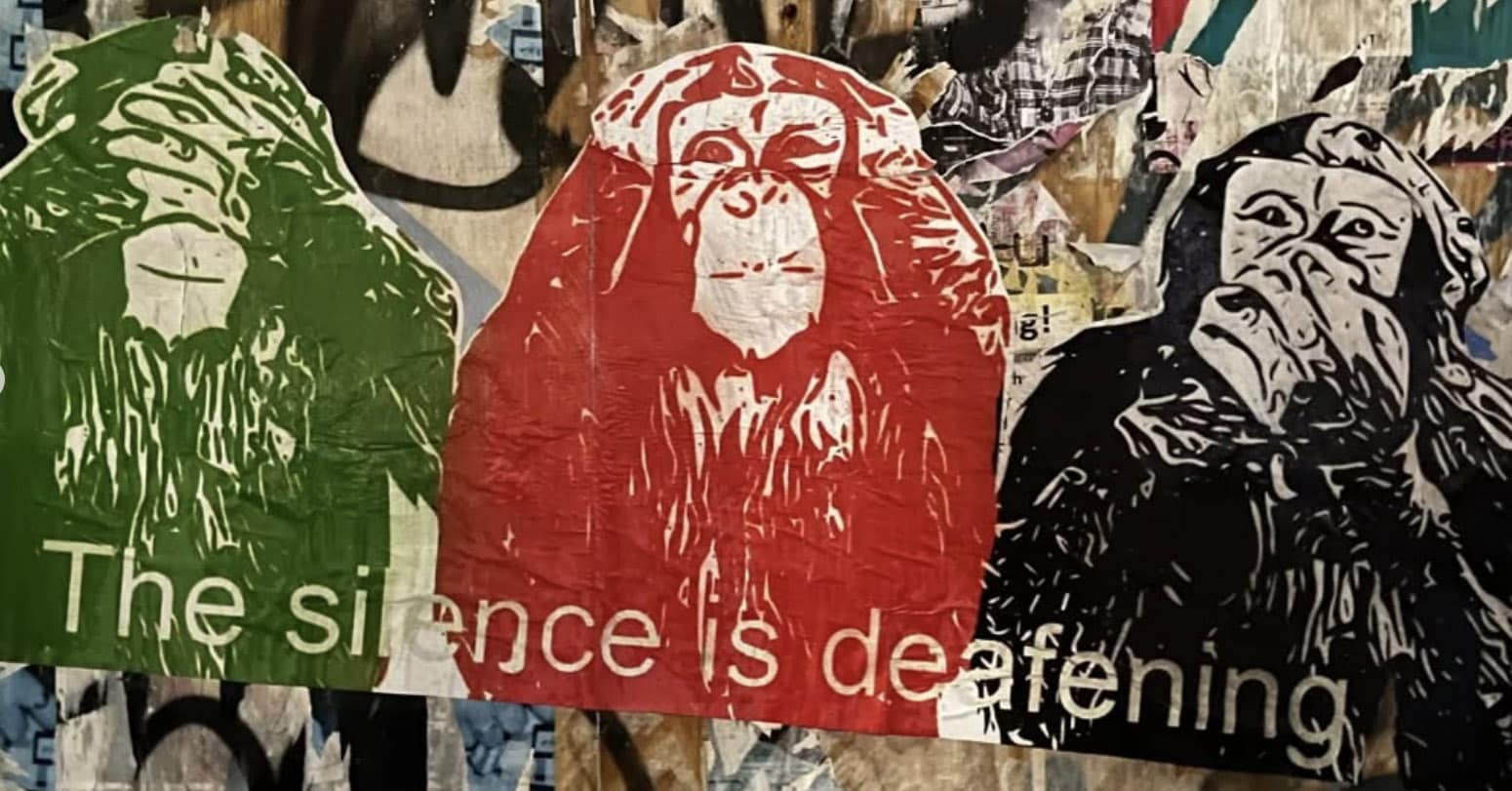 Tre stiliserte aper med hendene over øynene, ørene og munnen er avbildet på en graffitikledd vegg med teksten "Stillheten er øredøvende".