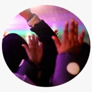 Flere barn i mørke jakker med hvite prikker rekker hendene i været i en fargerik, uskarp belysning.