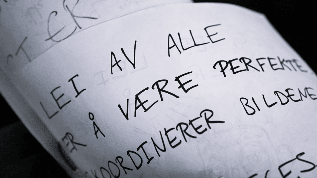 Nærbilde av håndskrevet norsk tekst på et hvitt papir, med noen ord delvis skjult av overlappende ark.
