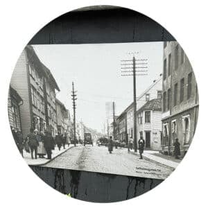 Svart-hvitt-foto av en bygate fra begynnelsen av 1900-tallet med gående mennesker, biler og trikker, trehus og strømstolper, merket "Solheimsgaten, 54.