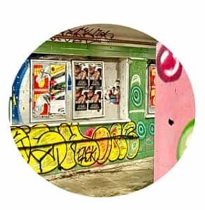 undergrunn En betongvegg dekket av fargerik graffiti og plakater er synlig gjennom en sirkelformet ramme mot en hvit bakgrunn.